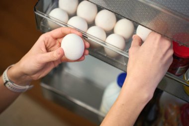 Dişi el, buzdolabının kapısındaki raftan taze yumurta alıyor içinde de diğer yumurta ve yiyecek kapları var. Ev mutfağında yemek pişirmek için tavuk yumurtası al.