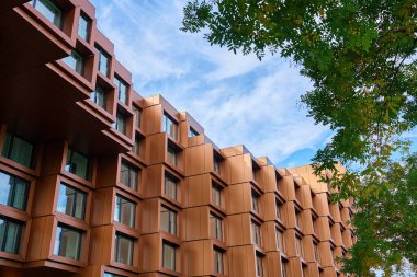 Modern bina cephesi, geometrik metal paneller ve ağaç dalları tarafından çerçevelenmiş mavi gökyüzünün altında geniş pencereler. Çağdaş mimari, şehir dışı ve ticari mülkiyet tasarımı kavramı