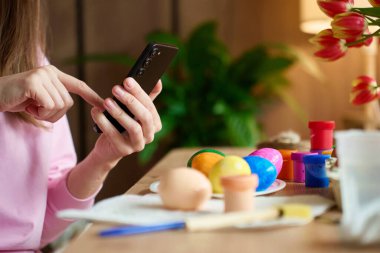 Paskalya yumurtalarını fotoğraflayan ve akıllı telefonlu el sanatları malzemeleri satan bir kadın. Tatil anları, sosyal medya ve dijital yaşam tarzını paylaşma kavramı.