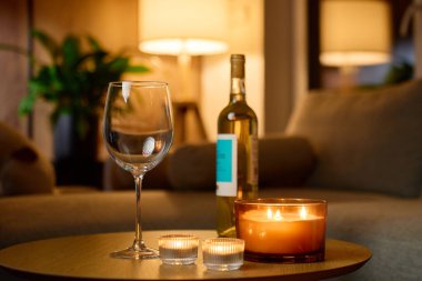 Boş şarap kadehi, bir şişe beyaz şarap ve sıcak oturma odasındaki masada yanan mumlar. Romantik akşam kavramı, randevu gecesi ve şarap.