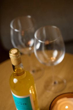 Bir şişe beyaz şarap ve iki boş şarap kadehi ev içi konforlu masada. Romantik yemek kavramı, randevu gecesi ve şarap içmek.