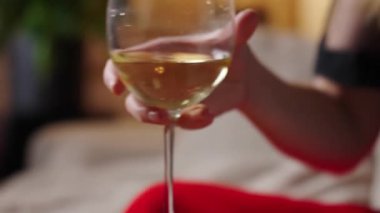 Kırmızı etekli bir kadın kanepede oturmuş, rahat oturma odasında mum ve hafif ışıklandırmayla beyaz şarap içiyor. İşten sonra rahatlama, akşam istirahatı ve stres atma kavramı