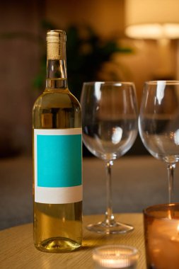 Beyaz şarap şişesi, iki boş şarap bardağı ve sıcak bir masada yanan mumlar. Romantik akşam kavramı, randevu gecesi ve evde rahatlama.