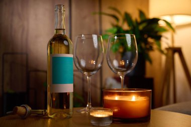 Beyaz şarap şişesi, iki boş şarap bardağı ve sıcak bir masada yanan mumlar. Romantik akşam kavramı, randevu gecesi ve evde rahatlama.