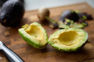 Çukurlu avokado yarıları, odun kesme tahtasındaki kırıntılar ve bıçaklar. Yemek hazırlama, sağlıklı yemek pişirme ve guacamole kavramı