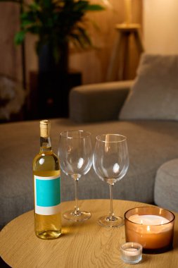 Beyaz şarap şişesi, iki boş şarap bardağı ve sıcak bir masada yanan mumlar. Romantik akşam kavramı, randevu gecesi ve evde rahatlama.