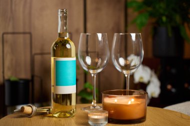 Bir şişe beyaz şarap, iki boş şarap bardağı ve sıcak ev içinde yanan mumlar. Romantik yemek kavramı, randevu gecesi ve şarap içmek.