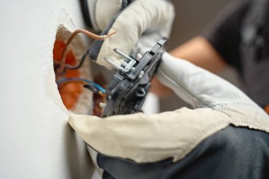 Elektrikçi elleri koruyucu eldiven takıyor ve bakır elektrik kablolarını duvar lambasına bağlıyor. Elektrik güvenliği, profesyonel onarım, ev yenileme ve bakım kavramı
