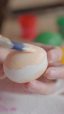 Beyaz yumurtayı bej boyayla boyayan bir kadın. Paskalya hazırlığı, yaratıcı hobi ve mevsimlik gelenek kavramı
