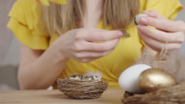 Süslü Paskalya yumurtaları tutan bir kadın. Tüylü ve ipli. Tahta masada, bahar laleleriyle. Paskalya hazırlığı, tatil dekorasyonu ve el yapımı süsler kavramı