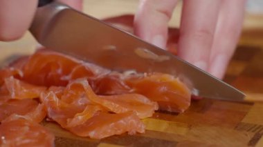 Ev mutfağında somon filetosunu tahta kesme tahtasının üzerinde bıçakla dilimleyen elleri kapatın. Yemek pişirme, yemek hazırlama ve sağlıklı kahvaltı kavramı.