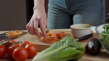 Ahşap kesme tahtasındaki avokado tostuna füme somon ekleniyor. Sağlıklı kahvaltı hazırlığı kavramı