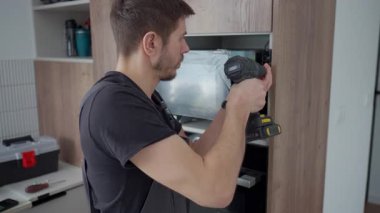 Çalışma kıyafetli bir adam, mikrodalga fırının üstüne kablosuz tornavida kullanarak ahşap mutfak dolabına yerleştirilmiş.