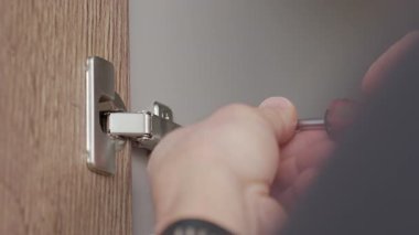 Eller tahta kapıdaki tornavidayla dolap menteşesini sıkılaştırır. Kabine menteşe kurulumu ve ev onarım bakımı kavramı.