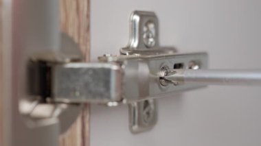 Ahşap dolap kapısındaki gizli metal menteşeyi sıkmak ya da ayarlamak için tornavida kullanın.