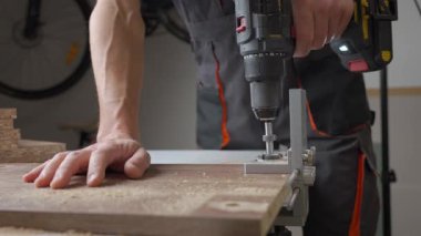 Marangozun ahşap tahtada matkap ve metal zımbırtı kullanarak delik açtığı yakın plan. Adam ev atölyesinde çalışıyor. Ahşap işçiliği ve mobilya montajı kavramı
