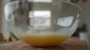 Elleri çırpılmış yumurtaları cam kasede çırpıyor. Ahşap mutfak tezgahında, yumurta kabuklarıyla. Kahvaltıyı hazırlayan kişi. Ev yemeği, yemek hazırlama ve tarif malzemeleri kavramı.