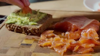 Avokado ekmeğine tütsülenmiş somon dilimlerini tahta kesme tahtasına koymak. Sağlıklı kahvaltı hazırlama, ev yapımı aperatif ve deniz ürünleri sandviçi kavramı..