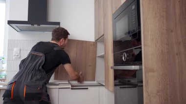 Modern apartman dairesine ahşap mutfak dolabı kapağı monte eden bir adam. Ev yenileme, mobilya montajı ve onarım hizmeti kavramı
