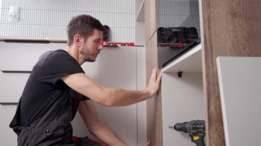 Mutfak kurulumu sırasında dolapta ahşap kapı paneli kuran iş kıyafetli adam. Tamirci evde kendi kendine mobilya monte ediyor.