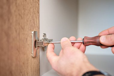 Ahşap mutfak dolabındaki tornavida kullanarak metal kapı menteşesini ayarlıyorum. Ev onarımı, mobilya kurulumu ve bakımı kavramı.