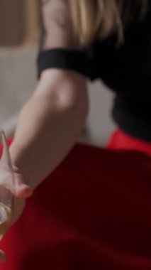 Kırmızı etekli bir kadın kanepede oturmuş, rahat oturma odasında mum ve hafif ışıklandırmayla beyaz şarap içiyor. İşten sonra rahatlama, akşam istirahatı ve stres atma kavramı