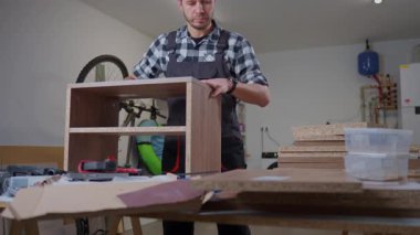 İş yerinde çalışan bir adam atölyede çip dolabının çerçevesini aletler ve tahtalarla birleştiriyor. Mobilya montajı, DIY yenileme ve marangozluk işi kavramı