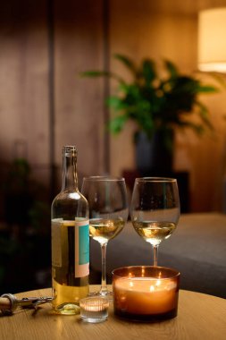 Beyaz şarap şişesi, iki boş şarap bardağı ve sıcak bir masada yanan mumlar. Romantik akşam kavramı, randevu gecesi ve evde rahatlama.