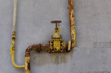Sıva kaplı bir duvarda eski, paslı, sarı bir musluk vanası. Çizgili gri duvar. Modası geçmiş tesisat. Sanayi geçmişi