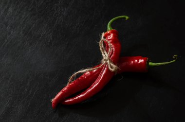 Siyah zemin üzerinde iki kapsül olgun kırmızı biber. Sebze bahçesinden taze koparılmış ve sicimle bağlanmış. Yeni acı biber mahsulü.