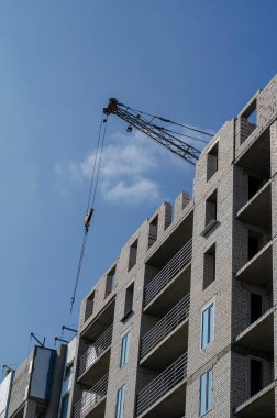 Mavi gökyüzüne karşı tamamlanmamış bir gökdelen. Cephe, binanın dış duvarlarının ısı ve nem yalıtımı üzerinde çalışıyor. İnşaat endüstrisi.