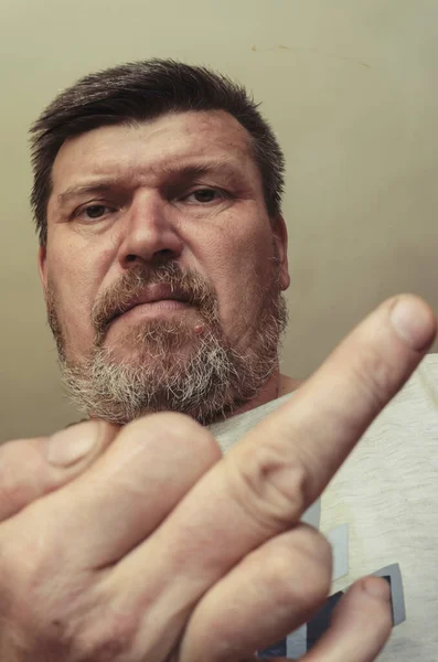 Unusual portrait of a man showing a middle finger gesture. An adult man with a beard makes a decent gesture and looks at the camera.