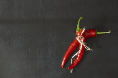 Siyah zemin üzerinde iki kapsül olgun kırmızı biber. Sebze bahçesinden taze koparılmış ve sicimle bağlanmış. Yeni acı biber mahsulü.