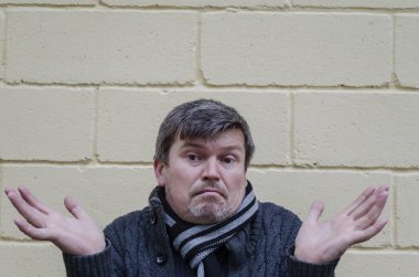 Elleri yandan boşanmış, şaşırmış bir adamın portresi. Orta yaşlı grimsi adam sarı arka plana şaşırdığını ifade etti.