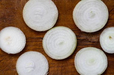 Çiğ ampul, tahta kesme tahtasındaki halkalarla dilimlenmiş. Bir ampul yedi parçaya bölündü. Yukarıdan görüntüle.