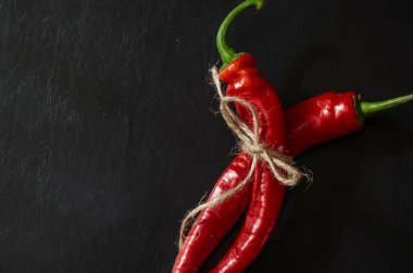 Siyah zemin üzerinde iki kapsül olgun kırmızı biber. Sebze bahçesinden taze koparılmış ve sicimle bağlanmış. Yeni acı biber mahsulü.