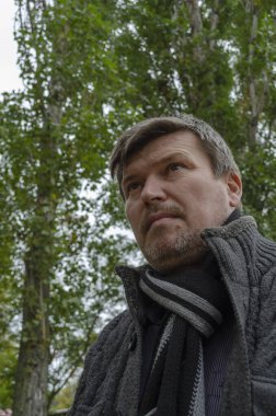 Gri tüyleri olan orta yaşlı bir adamın sonbahar parkındaki portresi. Boynunda gri örgü süveter ve atkı olan yetişkin bir adam..