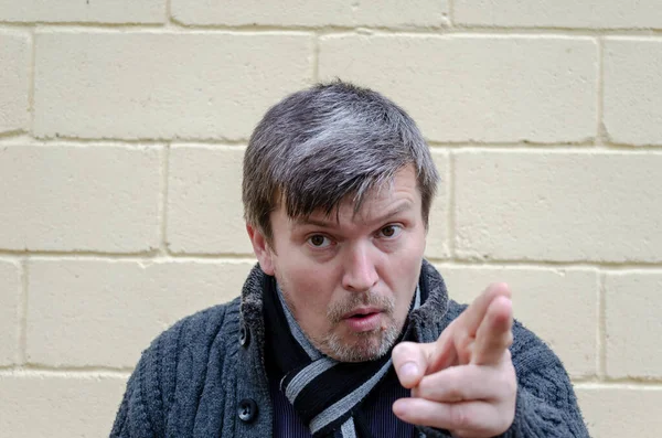 Öfkeli, el kol hareketi yapan bir adamın portresi. Orta yaşlı grimsi bir adam, sarı arka planda kızgın bir yüzle kameraya bakıyor..