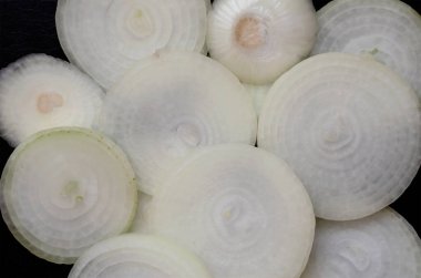 Siyah desenli arka planda halkalarla dilimlenmiş çiğ ampul. Beyaz ampul parçaları rastgele sıralanmış. Yukarıdan görüntüle.