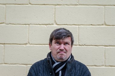 Yüzünde kibirli bir ifadeyle insan portresi. Küstah bir yüz ifadesi olan orta yaşlı, kır saçlı bir adam sarı duvar arkasına bakıyor..