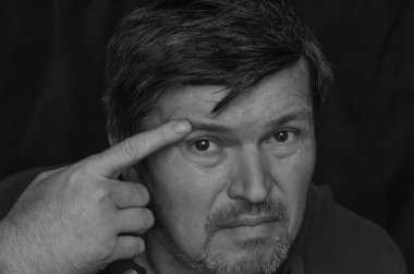 Vücut hareketleri konsepti. Elleriyle kaşlarına dokunan yetişkin bir adamın siyah beyaz portresi. Orta yaşlı bir adam kameraya yakından bakar ve işaret parmağıyla yüzüne dokunur..