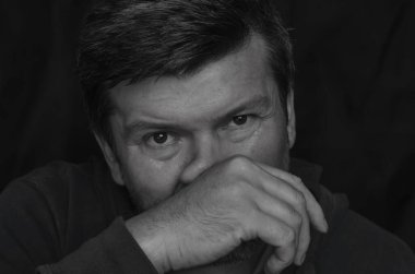 Vücut hareketleri konsepti. Yetişkin bir adamın siyah beyaz portresi eliyle burnunu ovuşturuyor. Orta yaşlı bir adam kameraya yakından bakıyor ve burnunu avucunun içine sürtüyor..