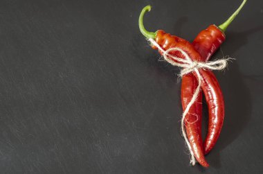 Siyah zemin üzerinde iki kapsül olgun kırmızı biber. Sebze bahçesinden taze koparılmış ve sicimle bağlanmış. Yeni acı biber mahsulü.