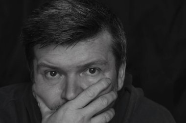 Vücut hareketleri konsepti. Yetişkin bir adamın siyah beyaz portresi eliyle ağzını kapatıyor. Orta yaşlı bir adam kameraya yakından bakar ve yüzünün alt kısmını avuç içiyle saklar..