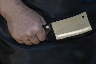 Bir adamın elindeki küçük mutfak baltası. Siyah önlüklü yetişkin adam mutfak bıçağı tutuyor..