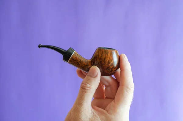 Briar root smoking pipe in hand. A man\'s hand holds a classic smoking pipe on a blue background. Selective focus.