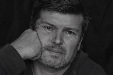 Vücut dili kavramı. Kafasını yumrukla destekleyen yetişkin bir adamın siyah beyaz portresi. Sıkılmış orta yaşlı bir adam..