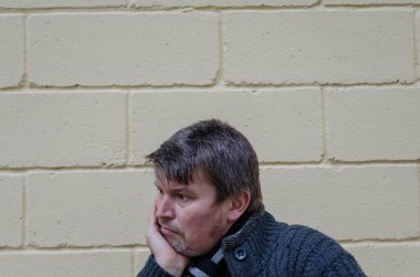 Çenesini avucunun içine koyan adamın portresi. Orta yaşlı grimsi bir adam sarı duvar arkasında düşünceli bir şekilde oturuyor..