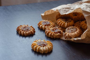 Kurabiyeler ve kağıt torba siyah masada. Kağıt ambalajından meyve reçeli dökülmüş lezzetli tatlılar. Şekerlemeci.