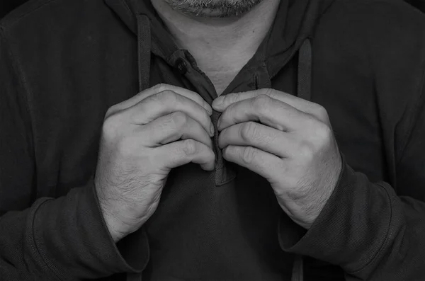 Man unbuttoned on  sports sweater. Middle-aged man\'s hands on cardigan collar with hood. Monochrome.